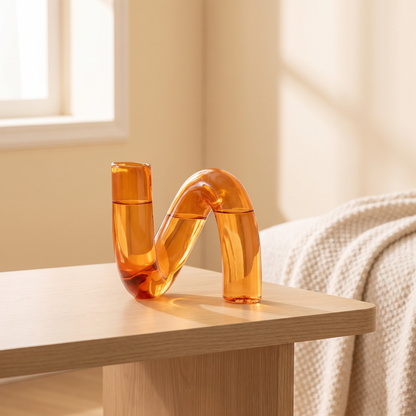 Irregular shaped amber glass vase on a wooden coffee table beside a cream throw blanket