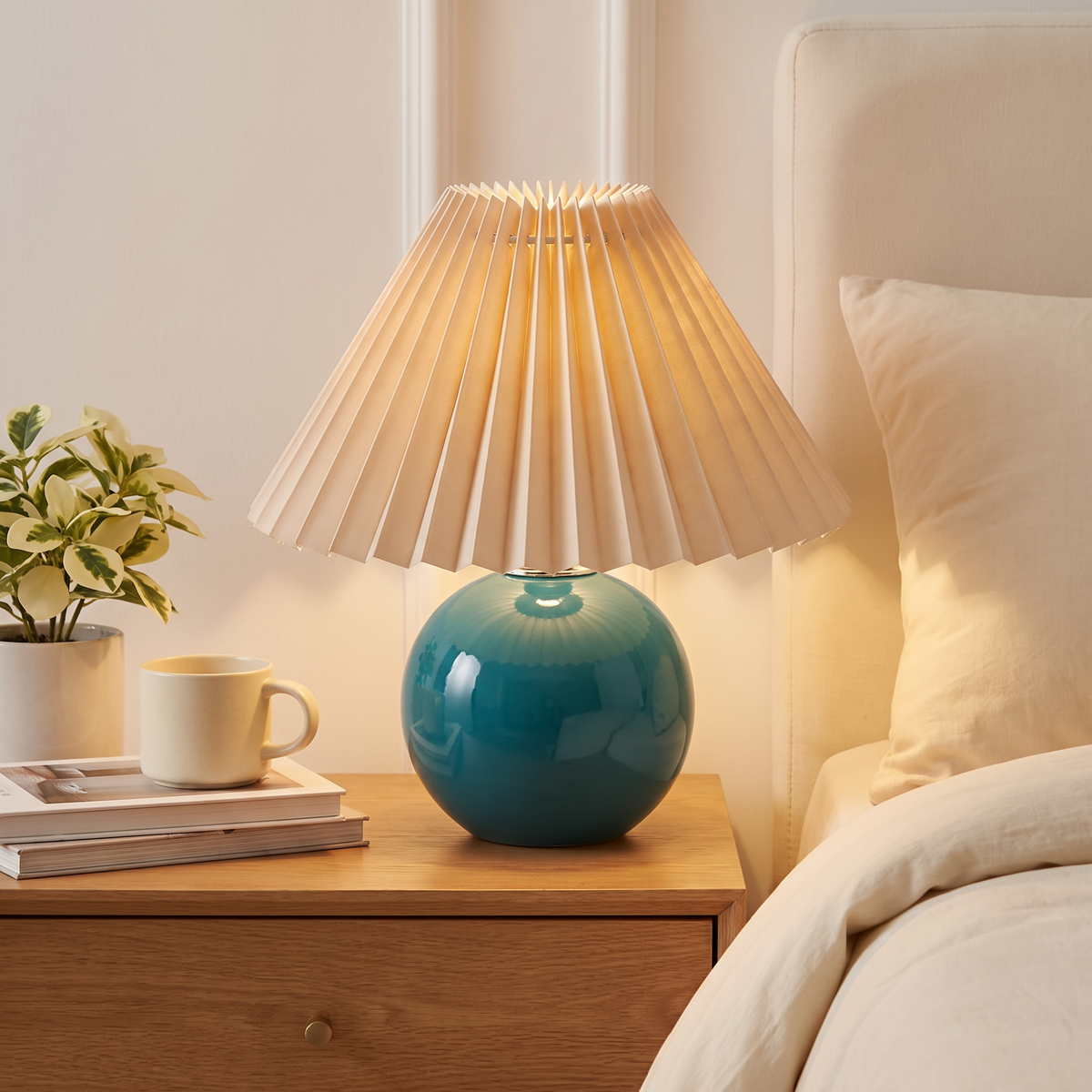 White ceramic table lamp with textile shade glowing softly on a bedside nightstand